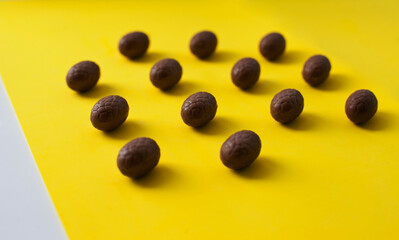 Easter colorful flat lay. Easter chocolate eggs of vibrant colors on bright yellow and white background.  Culture food and easter celebration pattern.