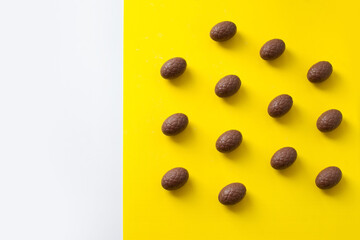 Easter colorful flat lay. Easter chocolate eggs of vibrant colors on bright yellow and white background.  Culture food and easter celebration pattern.