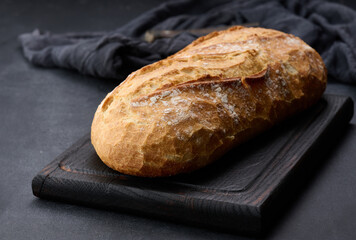 baked whole oval bread made from white wheat flour on a black table