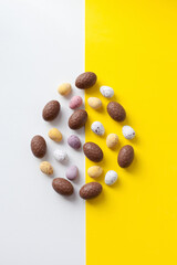 Easter colorful flat lay. Easter chocolate eggs in egg shape of vibrant colors on bright yellow and white background.  Culture food and easter celebration vertical flat lay.