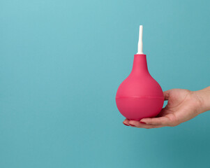 a hand in a blue medical glove holds a pink rubber enema on a blue background
