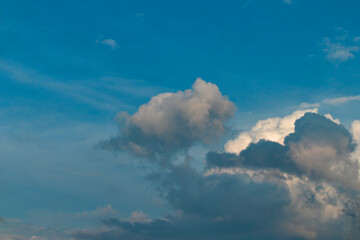 group of white clouds, some shaded in gray and orange, floating under a blue sky.
