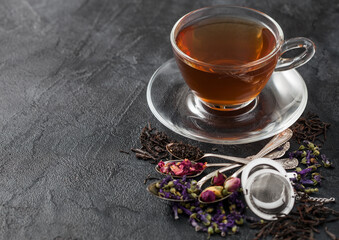 Glass tea cup with infuser and various tea on black background. Black and green loose tea,rose buds,blue mallow flowers