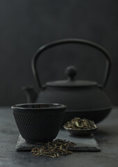 Chinese teapot with plate of loose black tea and cup on black background.