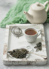 Green loose tea with tea ball strainer infuser and ceramic teapot with cup in wooden box with green cloth