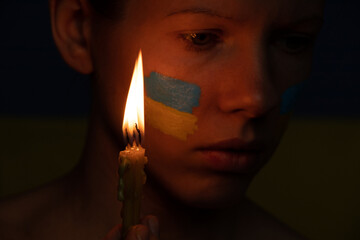 The girl's face with the national flag of Ukraine yellow-blue on the face of the background of the flame of a candle, peace in Ukraine, a prayer for the country