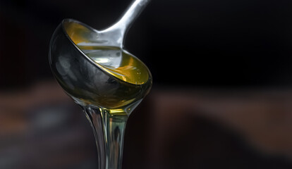 Yellow honey flows out of the scoop like a waterfall, against a blurry dark background. Close-up