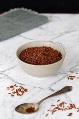 Red rice grains in a bowl. Whole grain rice heap on marble table.
