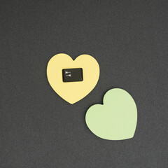The tab key on the pastel yellow heart-shaped sticky notepad. Pastel green heart-shaped sticky notepad next to. Black background. Minimalist concept of creative design. Flat lay.