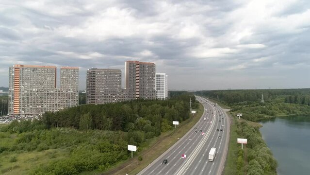 Aerial drone shot of apartment buildings next to the highway on cloudy day. Aerial shot over community apartment complex with parking and cars surrounded by forest. Gloomy cloudy sky. Lots of cars dri
