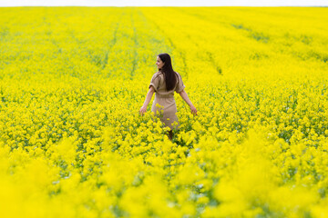 Fototapeta premium Happy woman walks run along yellow field rapeseed, hands raised to side enjoys nature. 