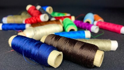 Multi-colored satin threads for sewing wound on spools of different sizes on a black table background