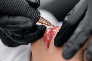Process applying permanent makeup tattoo of red on lips woman in beautician salon