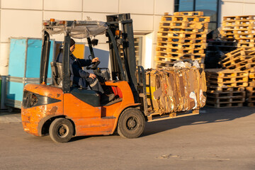 The forklift operator works on the territory of the store. Transportation of goods on a forklift truck. Waste paper loading, paper recycling plant.