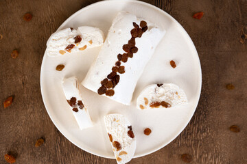 Traditional eastern sweets halva with raisin on a white plate. Wooden background. Top view. Selective focus.