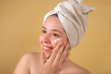 portrait young woman uses creams of her face. Isolated on a beige background. Happy healthy model skin care routine