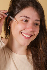 portrait young woman uses creams of her face. Isolated on a beige background. Happy healthy model skin care routine