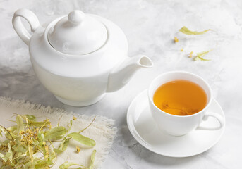a teapot and a cup with lime tea and flowers on a concrete table . Selective focus.