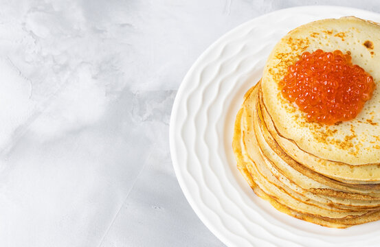 Pancakes for Maslenitsa with red caviar on a white plate. Top view with a place to copy.