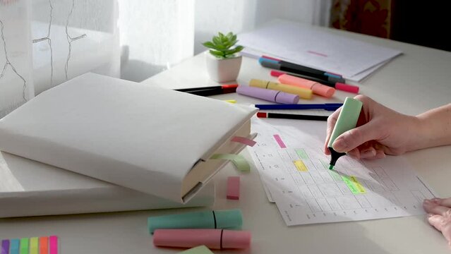 Scheduling and planning the week. Student time management. Women's hands write the schedule on a piece of paper and mark with a marker on a white table on a sunny day. Side view.