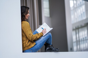 attractive brown hair student woman journaling thoughtful with pen in casual jeans outfit in a...