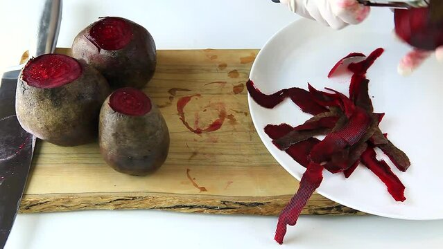 Cooking at home. Peeling raw beets with a vegetable knife. Hands in white gloves. Close-up.