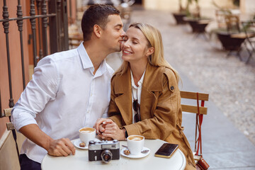 Loving man kissing his girlfriend on cheek during date in street cafe