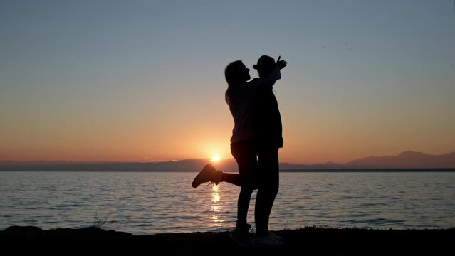Girlfriend covering eyes of her boyfriend from behind to surprise him, silhouettes of loving couple against sunset.