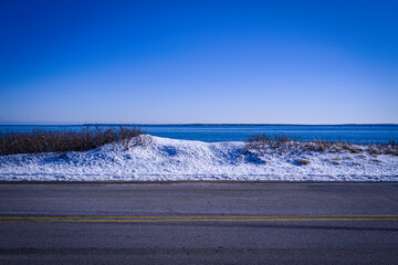 Tranquil seascape topography with the blue sky, sea, snow-covered sand dunes, wild plants, paved highway on the Cape Cod Coastal shoreline