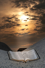 The Holy Bible open outdoors on top of a rock under the orange light of the sun at dawn