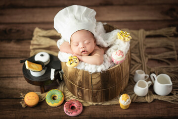 Happy adorable cute Asian newborn baby wearing chef hat sleeping with donuts prop