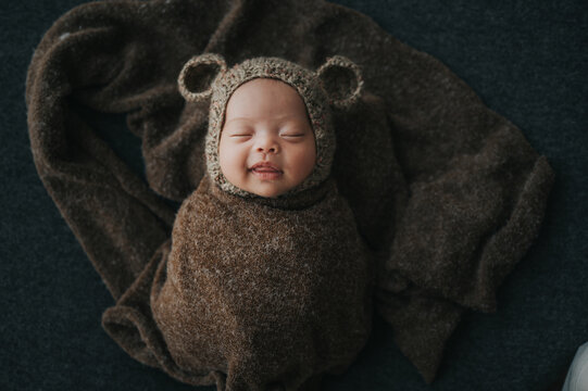 Happy newborn baby wrapped in cocoon sleeping with cute knit bear hat