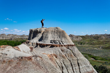 male person on the top of a mountain in badlands southern alberta eroding ancient rock with bright blue sky background
