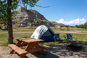 simple tent campsite with picnic table in Dinosaur provincial park southern alberta, grass and large rock formation in background with blue sky - obrazy, fototapety, plakaty