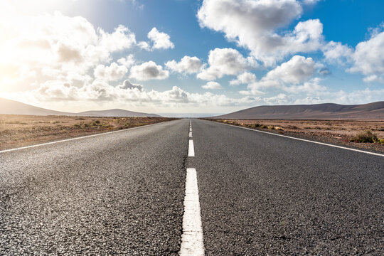 Straight of the infinite road, with the sea on the horizon with mountains in a arid landscape.