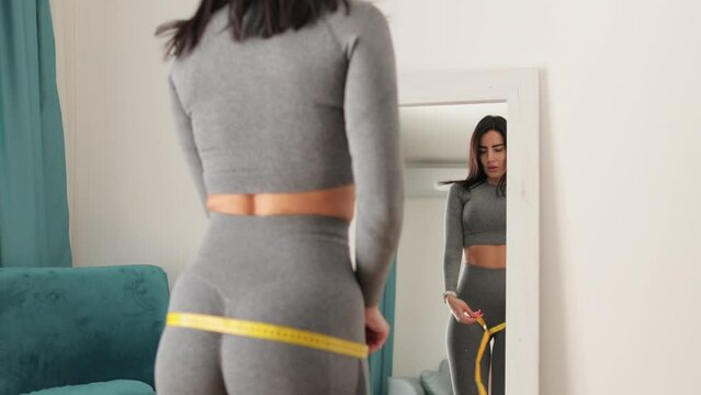slim Woman waist Measuring With Tape at home. Beautiful woman checking success of weight loss program and measuring body in living room. slimming and weight loss concept.