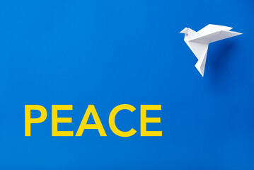 Word Peace in yellow on blue next to a white paper dove, symbol of peace