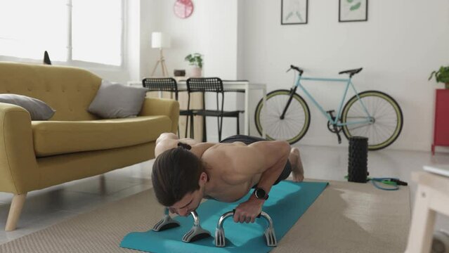 Young adult man doing push ups exercise in the living room at home - Healthy lifestyle and indoor workout concept
