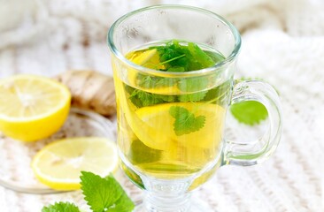 medicinal tea with lemon, lemon balm and ginger in a transparent glass on a light background, tea for colds and viruses