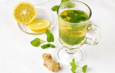medicinal tea with lemon, lemon balm and ginger in a transparent glass on a light background, tea for colds and viruses
