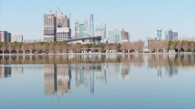 4k Time lapse footage of Shanghai city landmarks in sunny day with reflections in peaceful lake, tourists walking along lakeside and cranes moving on top of buildings.