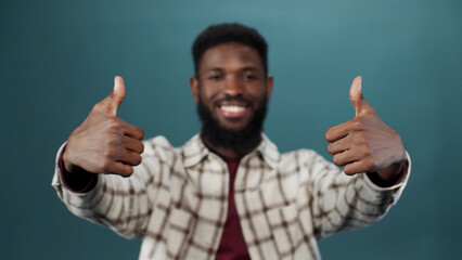 Carefree stylish dark-skinned young guy in checkered shirt with thumbs-up sign