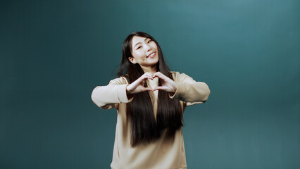 A handsome asian woman is showing a heart from her hands 