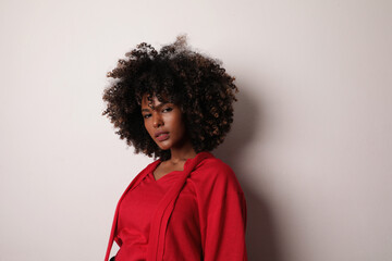 African American woman with curly hair wearing red top over white background.