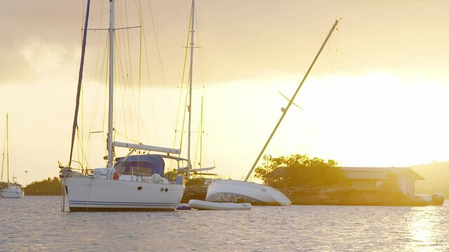 Wrecked sailboat overturned in the water in a small bay on the Caribbean island of Curacao at sunset.