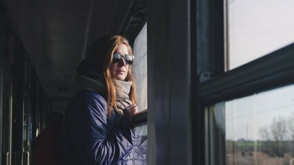Blonde Caucasian Female Travelling on High Speed Passenger Train Looking at Landscapes Through Window of Railroad Car	