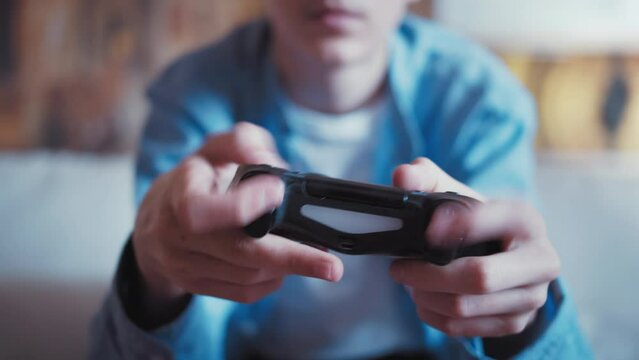 teen boy sitting on the sofa and playing a game on a console, joystick close-up, cinematic shot