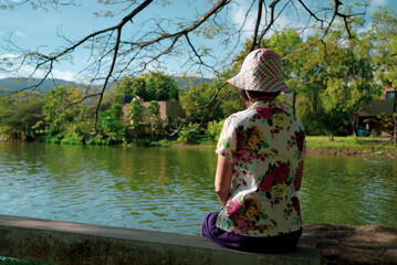 Rear View of Senior Woman Sitting by Lake and Enjoying Nature
