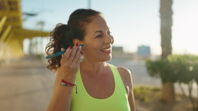 Middle age woman wearing sportswear listening audio message by the smartphone at street