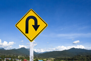 Traffic sign: Right U-turn sign on cement pole beside the rural road with white cloudy bluesky background, copy space.